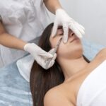 Closeup of the doctor with a scalpel treating the woman's skin. Dermaplaning treatment.