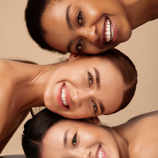 Three Multicultural Ladies Posing Smiling To Camera Over Gray Background. Multiethnic Female Beauty Portrait, Vertical